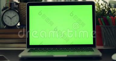 绿色屏幕笔记本电脑的多利拍摄。 黑暗的办公室。 完美地放置你自己的图像或视频。 正在使用的绿色技术屏幕